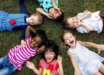En grupp glada barn ligger på rygg i gräset.